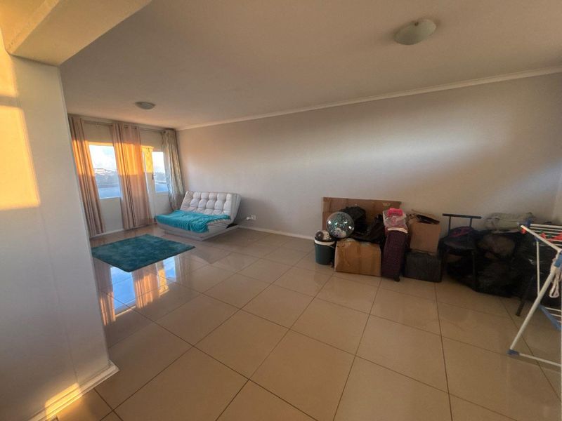 Spacious living area featuring large format floor tiles, neutral wall finishes, and a sliding glass door providing natural light.