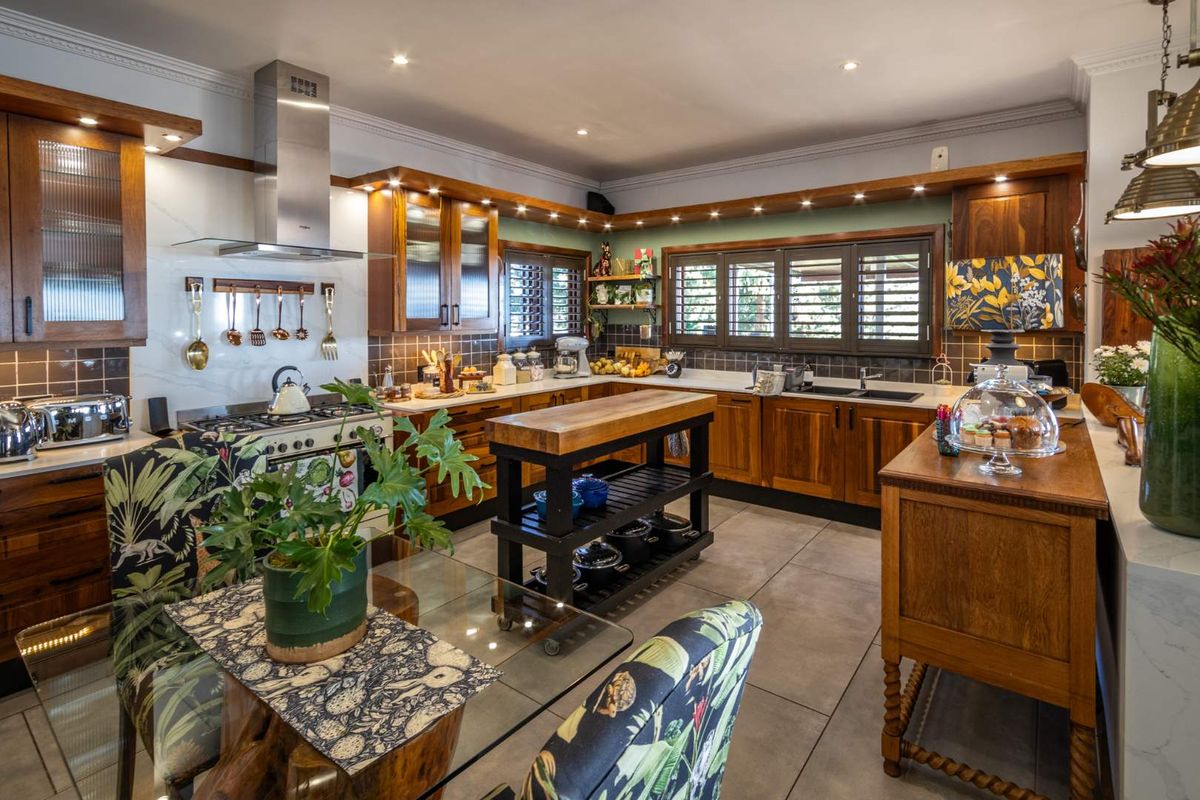 A well-appointed kitchen featuring warm wooden cabinetry, a gas stove with stainless steel extractor, tiled backsplash, and plantation shutters, offering a classic farmhouse aesthetic.