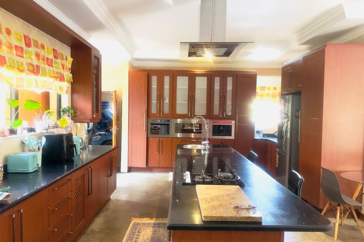 Spacious kitchen featuring dark wood cabinetry, a large central island with a built-in gas hob, and integrated stainless steel appliances.