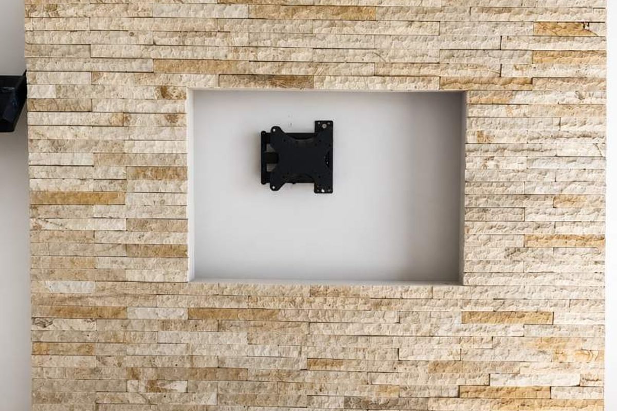 A feature wall finished in natural stacked stone, featuring a recessed niche with a mounted television bracket, set above tiled flooring.