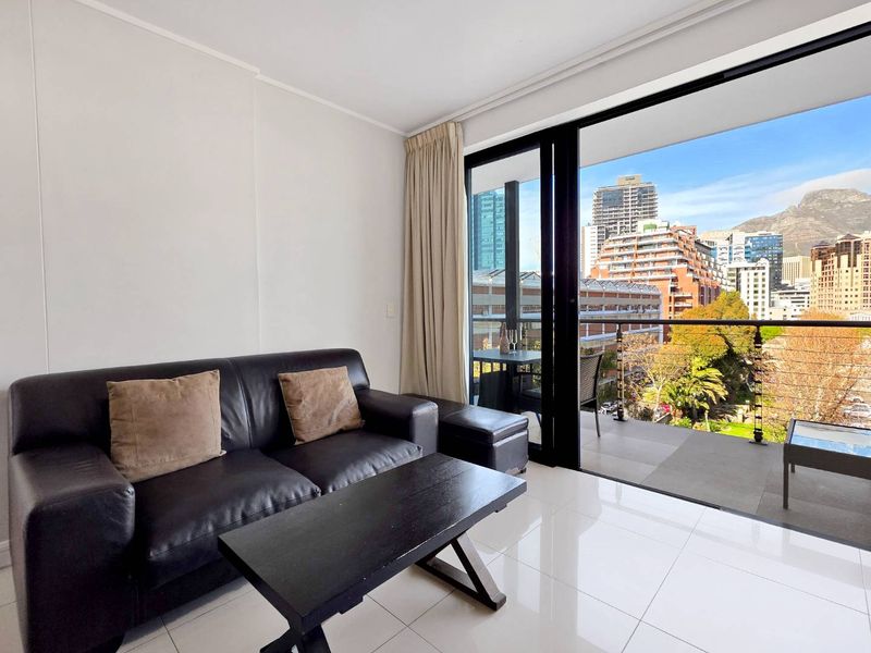A bright living room featuring large sliding glass doors that open onto a balcony with expansive city and mountain views.