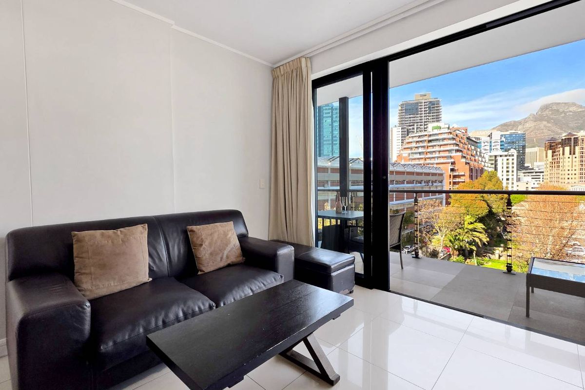 A bright living room featuring large sliding glass doors that open onto a balcony with expansive city and mountain views.
