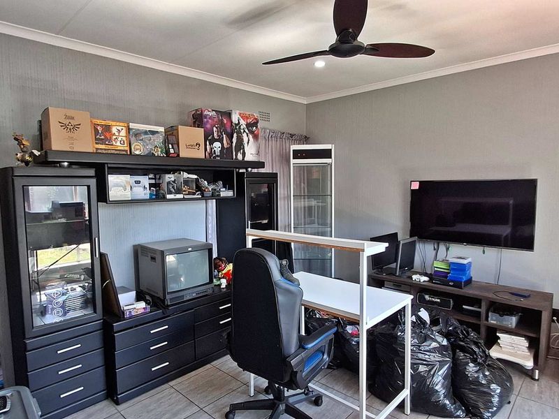 A living room featuring tiled flooring, a ceiling fan, and an arched doorway, currently utilized as a multi-purpose hobby and media space.