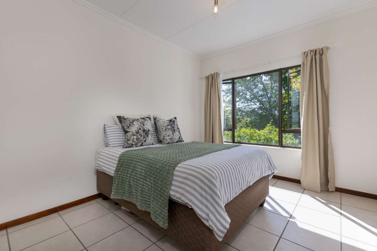 A bright bedroom featuring large windows with garden views, tiled flooring, and neutral wall finishes.