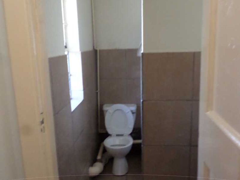 A small, functional bathroom featuring tiled walls and flooring with a standard toilet and visible plumbing fixtures.