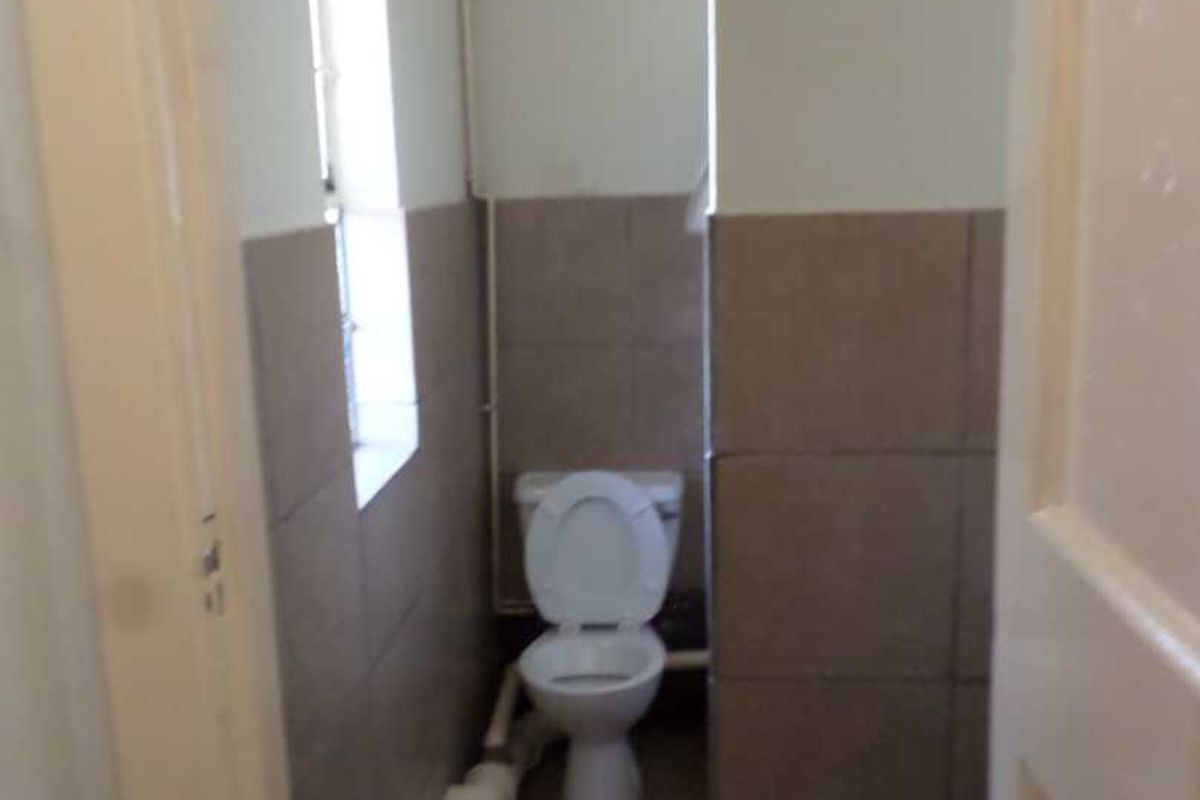 A small, functional bathroom featuring tiled walls and flooring with a standard toilet and visible plumbing fixtures.