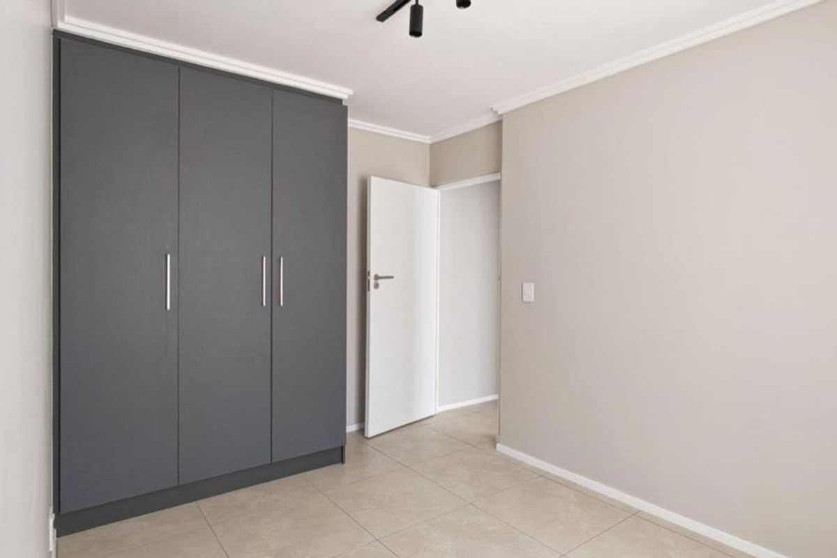 A clean, neutral bedroom featuring modern grey built-in cupboards, tiled flooring, and a simple interior door leading to the hallway.