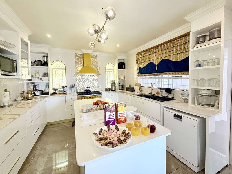 A bright, well-maintained kitchen featuring white cabinetry, stone countertops, a central island, and modern built-in appliances with a decorative tiled backsplash.