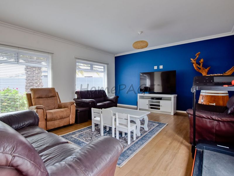A bright living room featuring laminate flooring, venetian blinds, and a bold blue accent wall, providing a comfortable and functional family space.