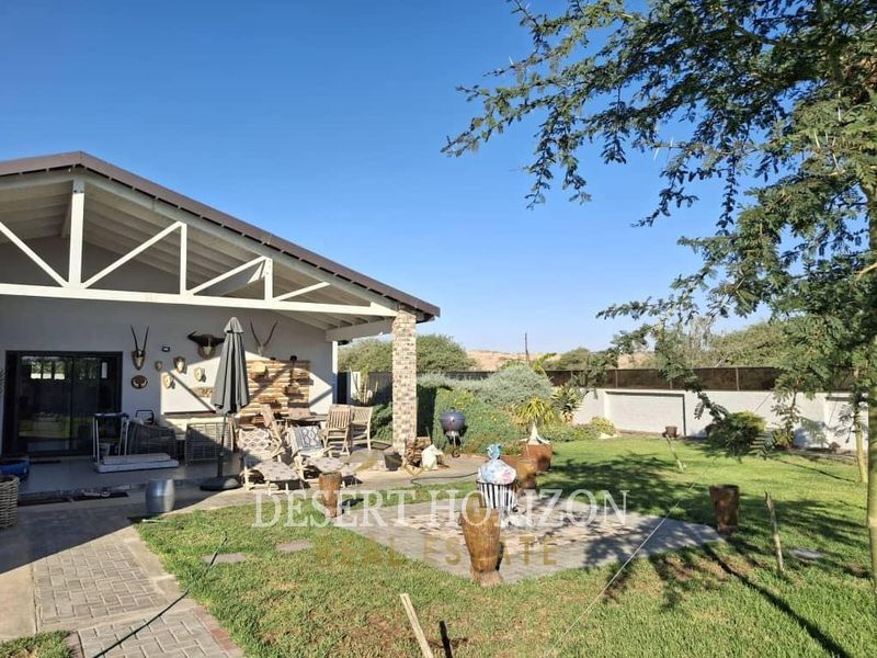 A spacious covered patio area overlooking a well-maintained garden with paved pathways and a solid boundary wall, ideal for outdoor entertaining.