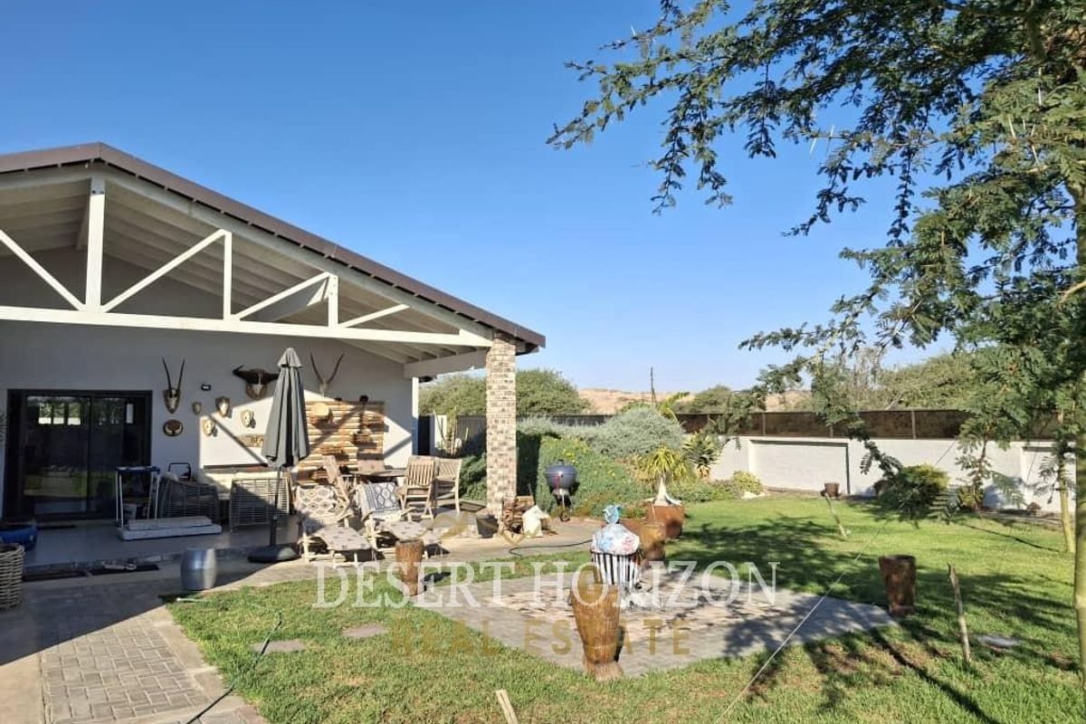 A spacious covered patio area overlooking a well-maintained garden with paved pathways and a solid boundary wall, ideal for outdoor entertaining.
