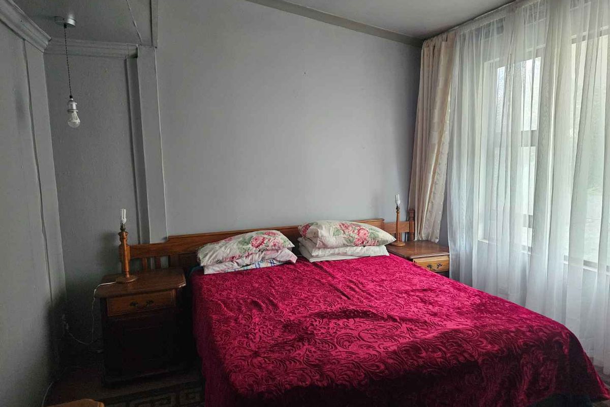 A bedroom featuring a built-in wooden headboard and bedside units, with visible wear to the ceiling and wall finishes.
