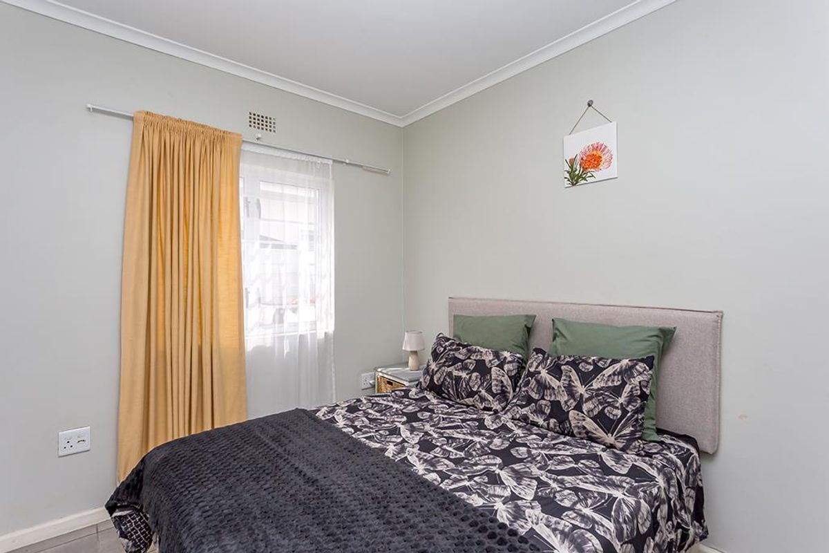 A well-maintained bedroom featuring neutral wall tones, a window with curtain rails, and standard electrical fixtures.