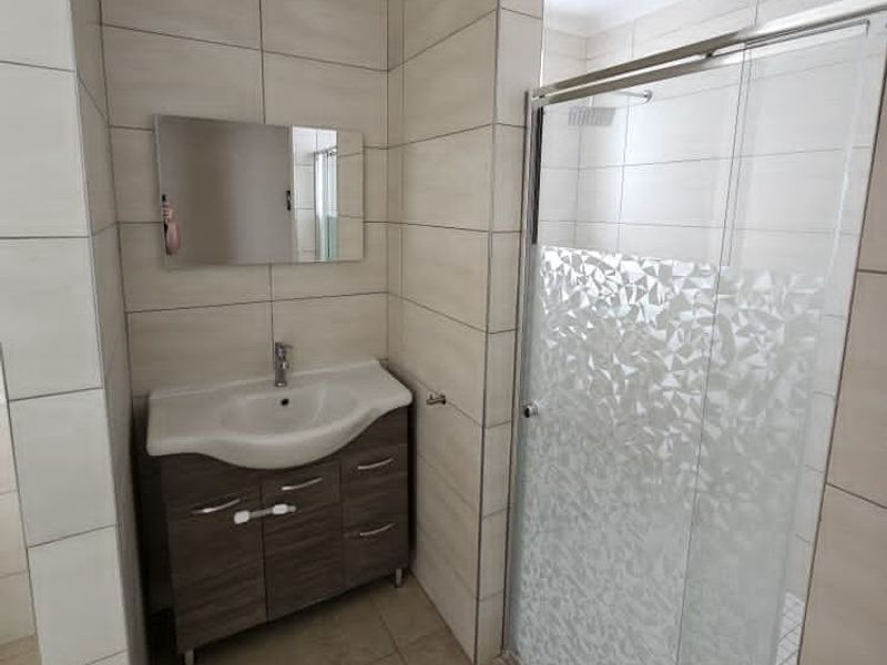 A modern bathroom featuring a vanity cabinet with a ceramic basin, a wall-mounted mirror, and a glass-enclosed shower with tiled finishes.