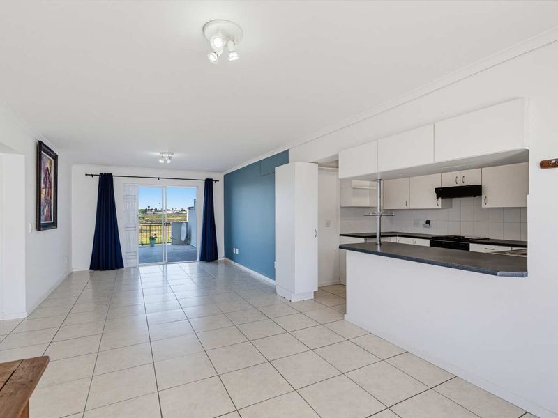 Open plan living and kitchen area featuring tiled flooring, a breakfast bar, and sliding glass doors leading to an outdoor balcony.