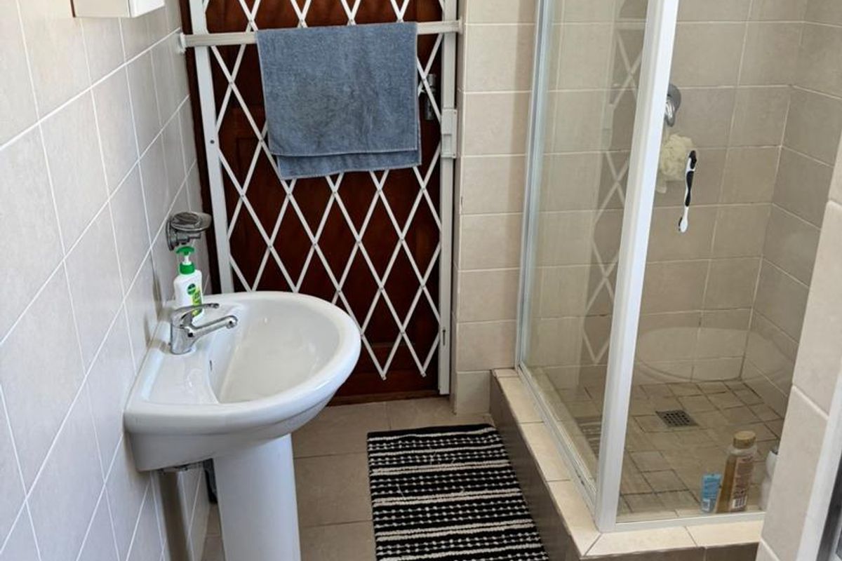 A functional bathroom featuring a pedestal basin, a tiled shower enclosure with a glass door, and a security gate at the entrance.