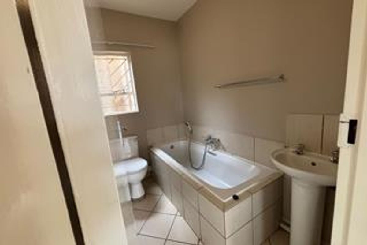 A functional bathroom featuring a standard bathtub, pedestal basin, and toilet with tiled flooring and neutral wall finishes.