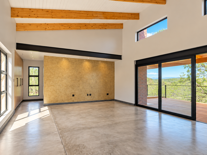 Spacious living area featuring polished concrete floors, exposed timber beams, a textured feature wall, and large sliding doors opening onto a wooden deck.