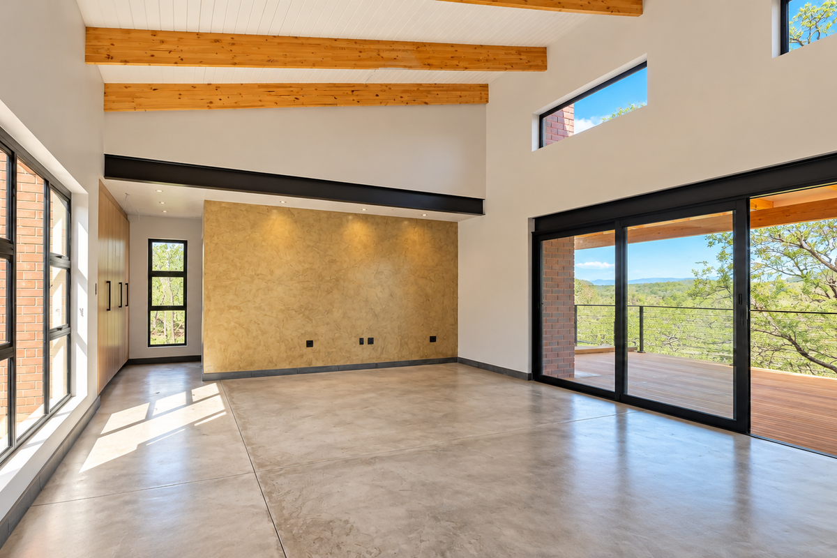 Spacious living area featuring polished concrete floors, exposed timber beams, a textured feature wall, and large sliding doors opening onto a wooden deck.