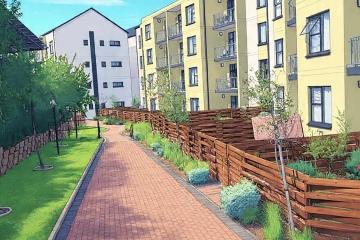 A well-maintained exterior view of a townhouse complex featuring a paved walkway, landscaped garden areas, and timber fencing between units.