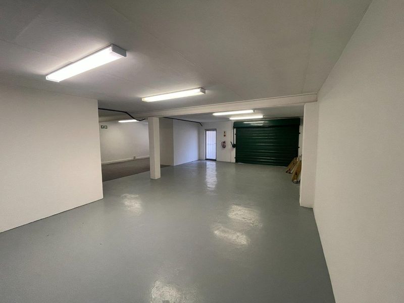 Spacious, clean garage area featuring an epoxy-coated floor, roller shutter door, and bright overhead fluorescent lighting, suitable for vehicle storage or utility use.