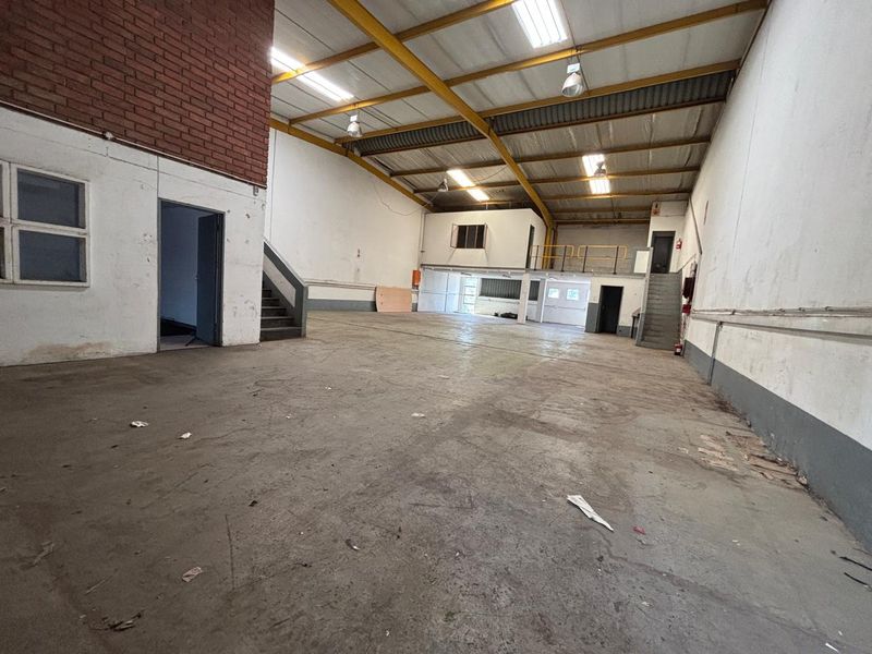 Spacious industrial warehouse unit featuring high ceilings with exposed steel trusses, a mezzanine level, concrete flooring, and functional staircase access.