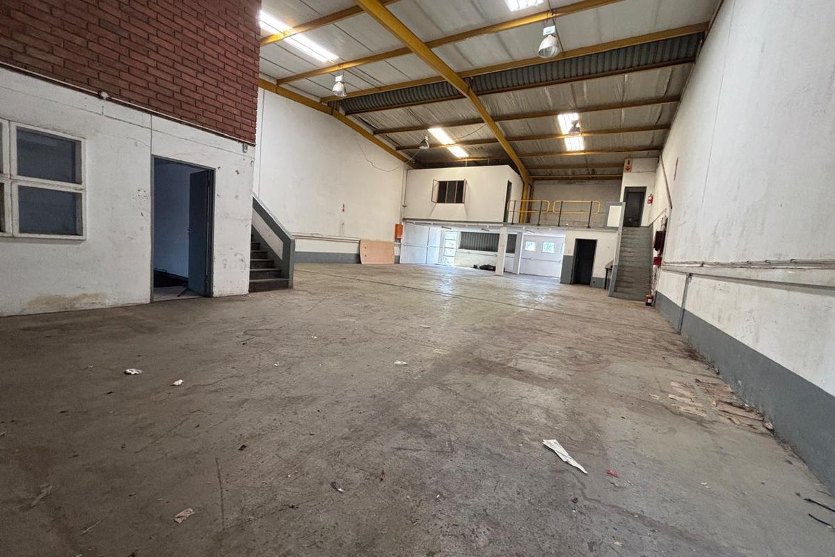 Spacious industrial warehouse unit featuring high ceilings with exposed steel trusses, a mezzanine level, concrete flooring, and functional staircase access.