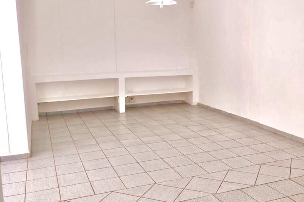 An empty, neutrally finished living area featuring tiled flooring, built-in shelving, and a simple pendant light fixture.