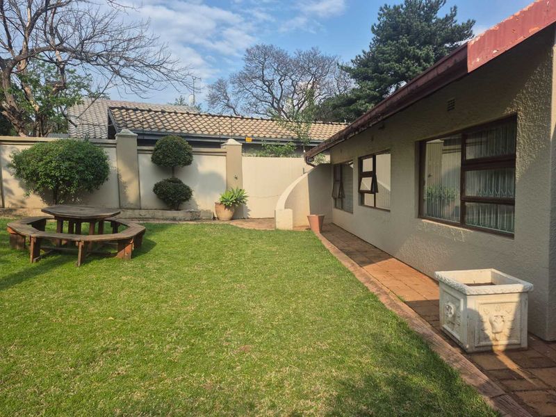 A private rear garden featuring a well-maintained lawn, perimeter wall, and a paved patio area adjacent to the house.