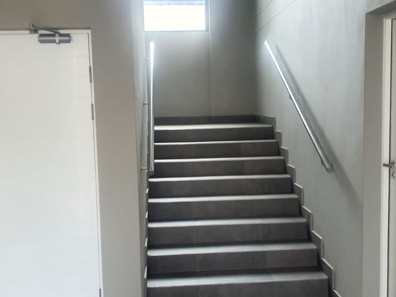A clean and modern apartment building hallway featuring a tiled staircase with metal handrails and secure access doors.