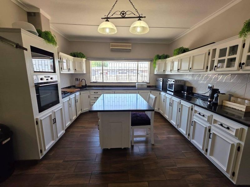 A well-appointed kitchen featuring white cabinetry, dark granite countertops, a central island, built-in oven and microwave, and durable wood-look tiled flooring.