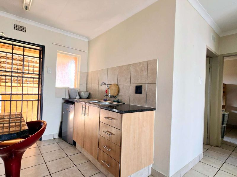 A compact kitchen area featuring light wood cabinetry, granite countertops, a stainless steel sink, and neutral tiled splashbacks with matching floor tiles.