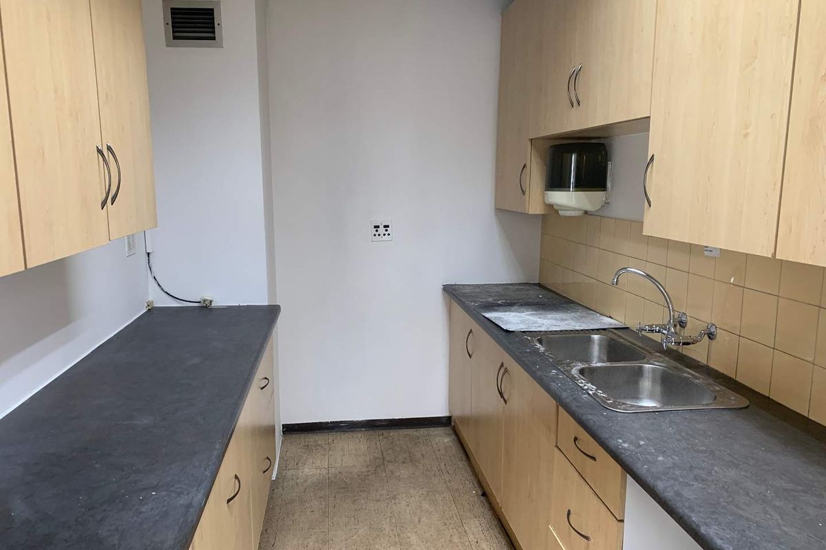 A functional kitchenette featuring laminate cabinetry, double stainless steel sink, tiled splashback, and dark laminate countertops in an industrial office setting.