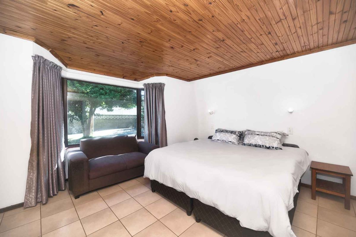 Spacious bedroom featuring a distinctive timber-clad ceiling, large window providing natural light, and neutral tiled flooring.