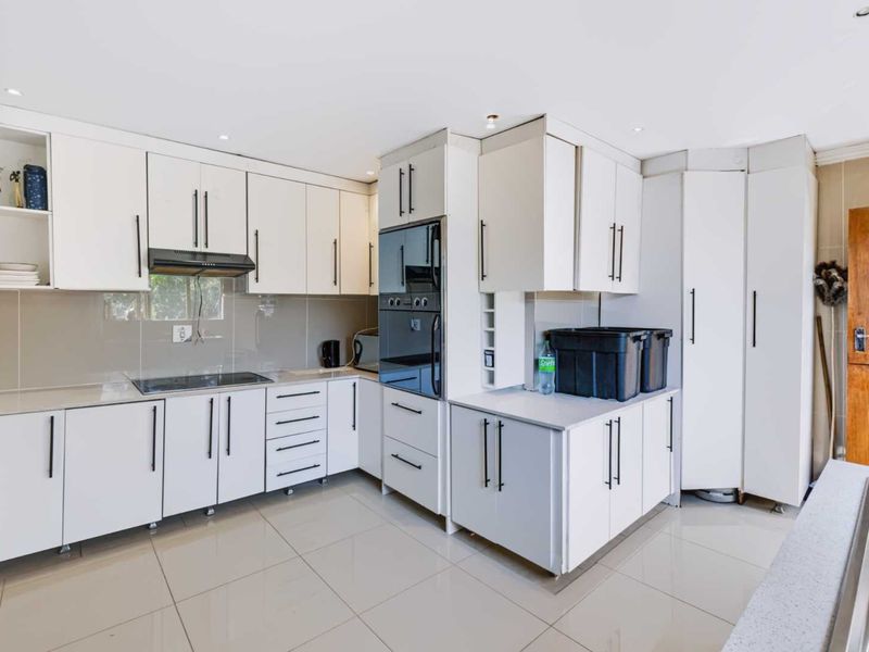 Modern kitchen featuring white cabinetry, stone countertops, integrated oven, electric hob, and sleek tiled flooring with recessed lighting.