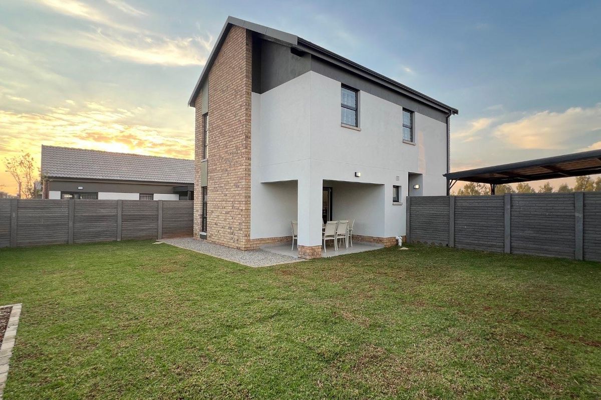 Rear view of a modern two-story house featuring a covered patio, landscaped lawn, and perimeter boundary walling.