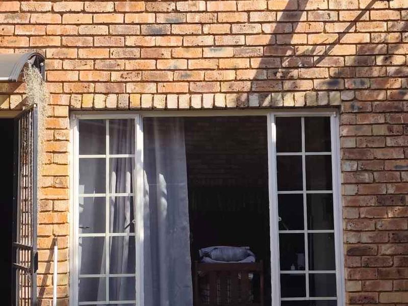 A view of the rear face brick facade of the townhouse, featuring a satellite dish, security gate, and window frames.
