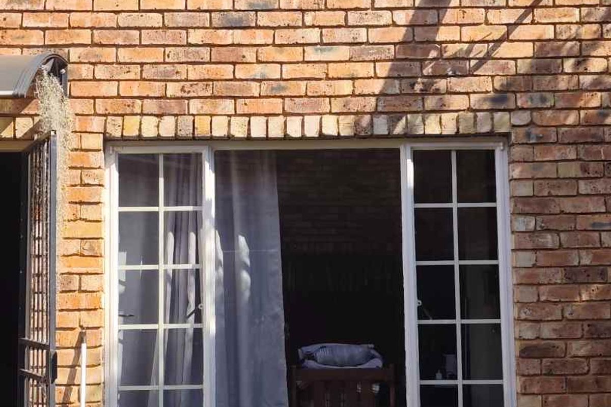 A view of the rear face brick facade of the townhouse, featuring a satellite dish, security gate, and window frames.