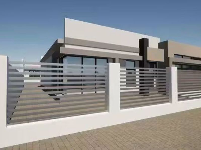 A modern residential property featuring a contemporary facade and a secure horizontal slat metal fence with masonry pillars.