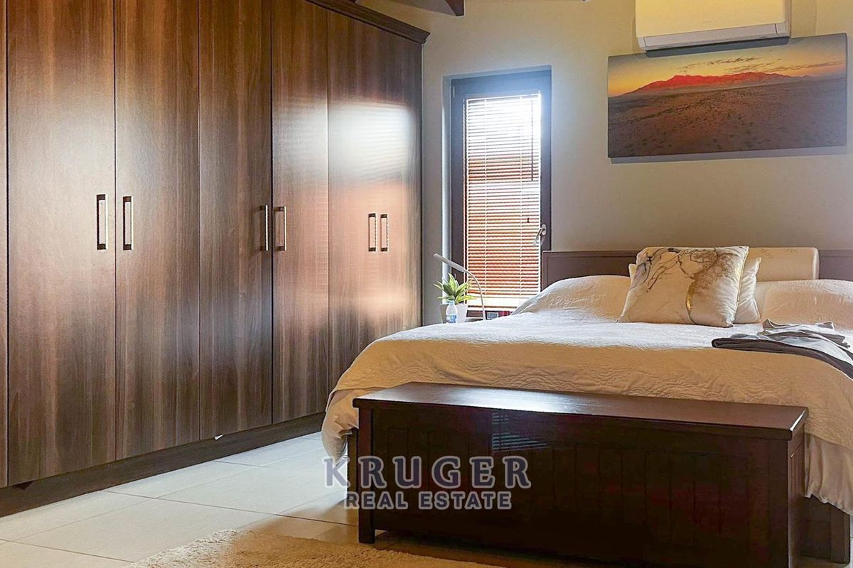 A well-maintained bedroom featuring extensive built-in wooden cabinetry, tiled flooring, and a wall-mounted air conditioning unit.