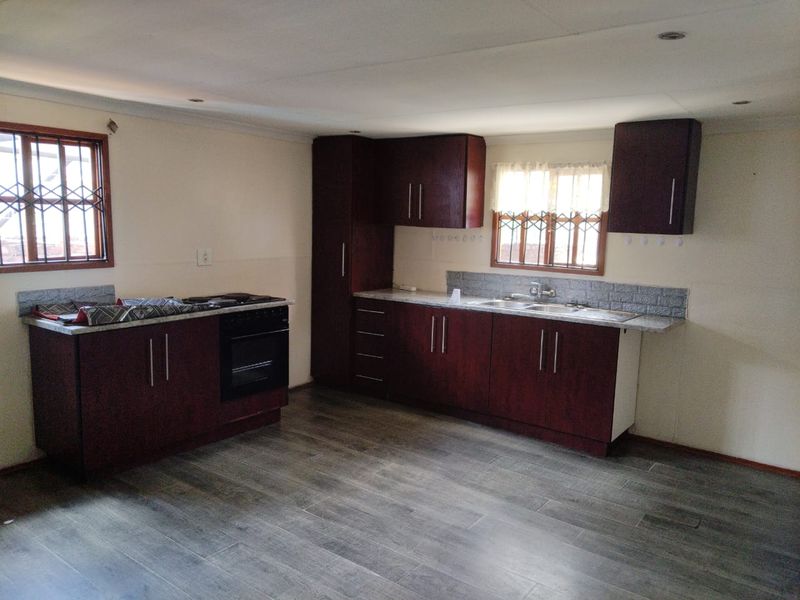 A functional kitchen featuring dark wood cabinetry, laminate countertops, a built-in oven and hob, and tiled flooring with security bars on the windows.