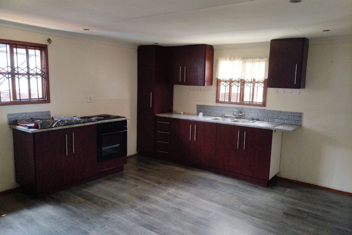 A functional kitchen featuring dark wood cabinetry, laminate countertops, a built-in oven and hob, and tiled flooring with security bars on the windows.