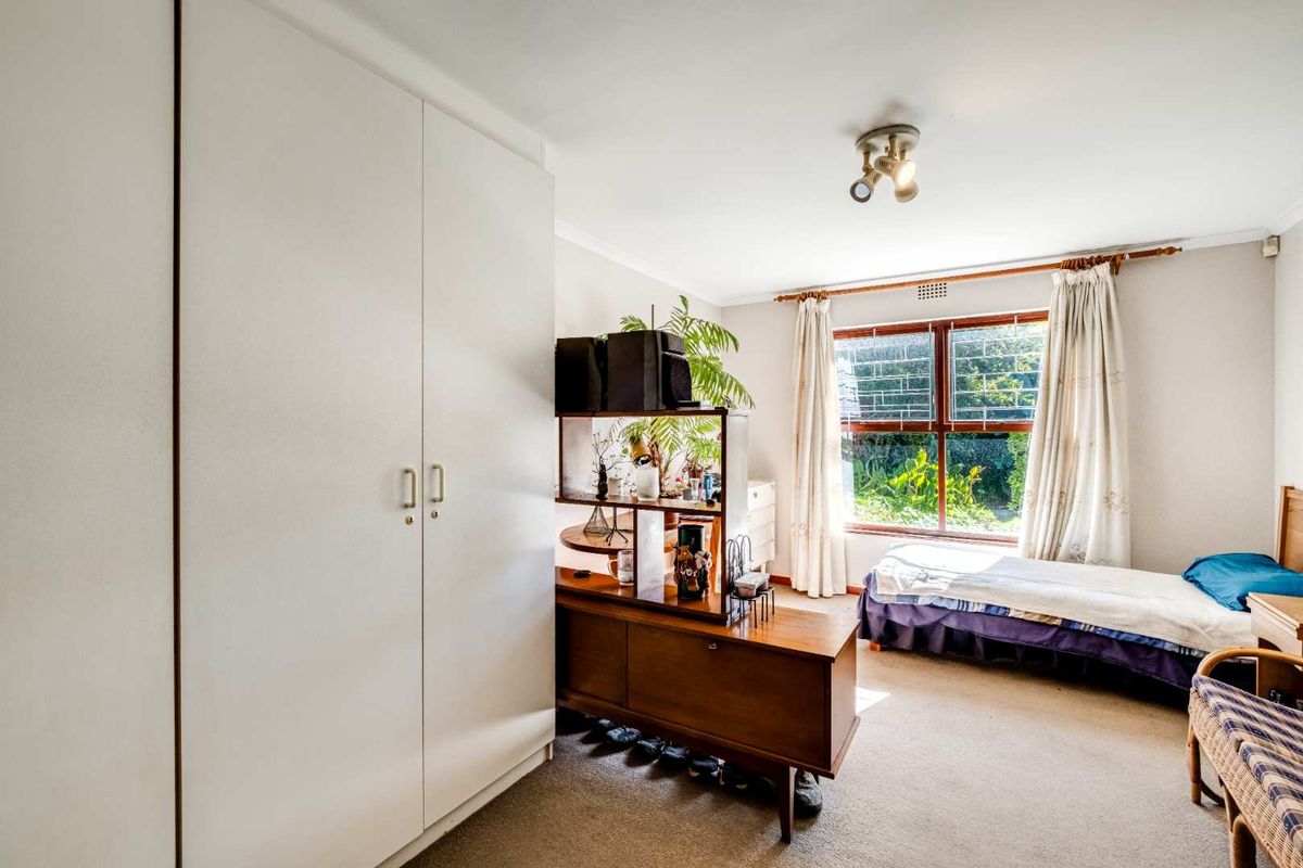 A well-lit bedroom featuring built-in wardrobes, carpeted flooring, and a large window overlooking the garden.