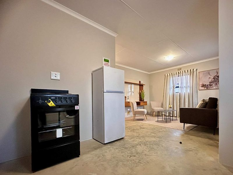 Open-plan living area featuring a basic kitchen zone with a freestanding stove and a connected lounge space with neutral wall finishes.