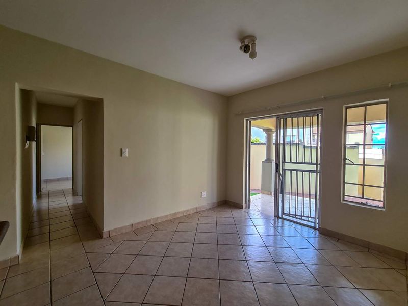 An empty living room featuring ceramic tile flooring, a sliding glass door with a security gate, and access to an outdoor patio area.