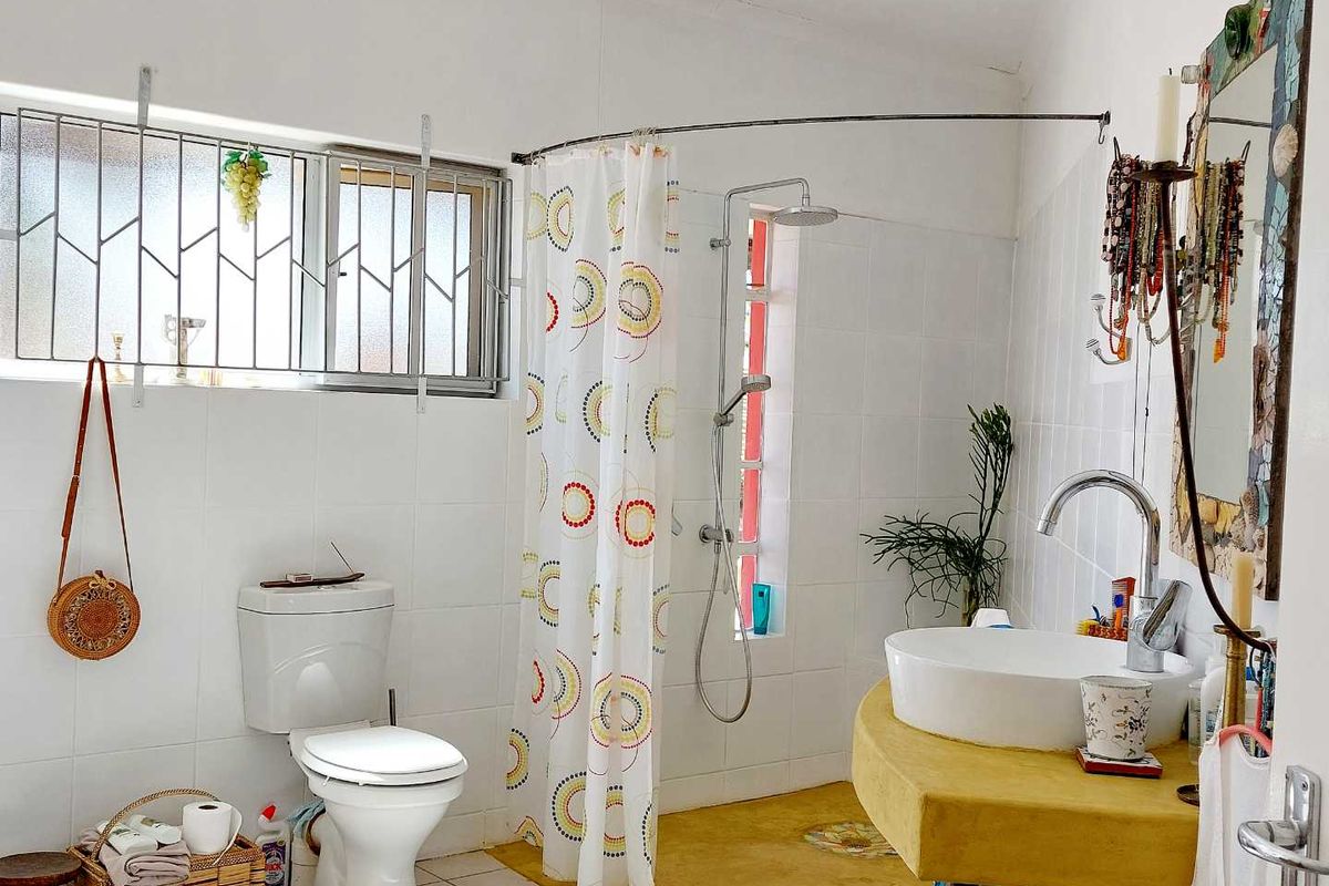 A functional bathroom featuring a white ceramic toilet, a vessel sink on a yellow vanity, and a shower area with a curtain.