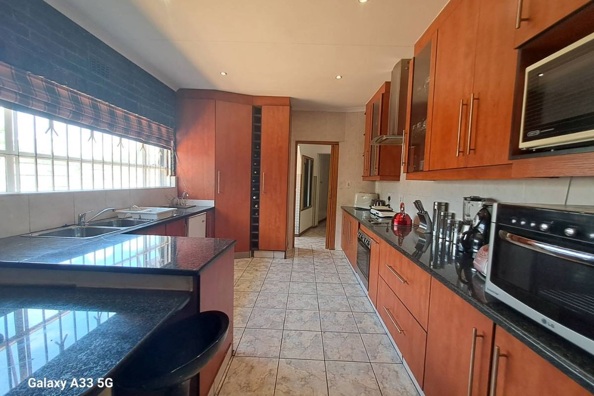 A functional kitchen featuring dark granite countertops, wood-veneer cabinetry, built-in oven, extractor fan, and tiled flooring with a breakfast bar area.