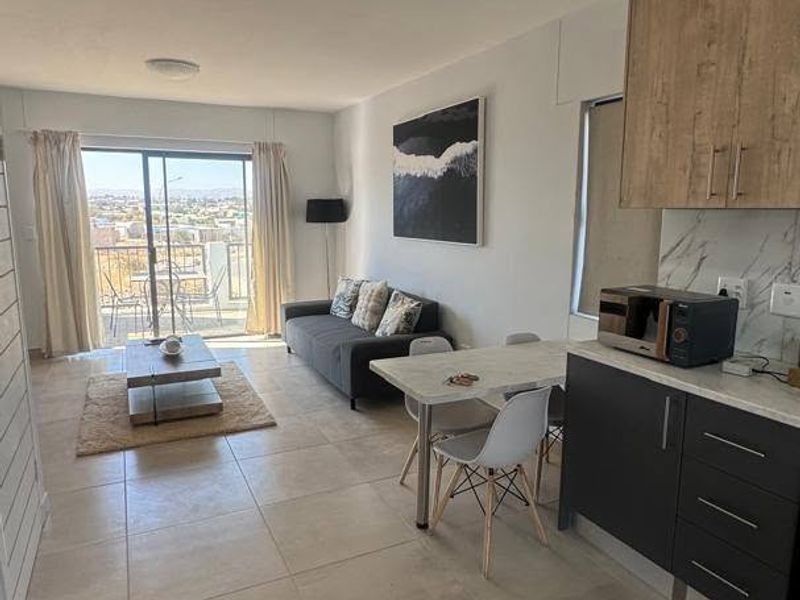 Modern open-plan living area featuring tiled floors, a contemporary kitchen with built-in cabinetry, and a sliding door leading to a balcony with scenic views.