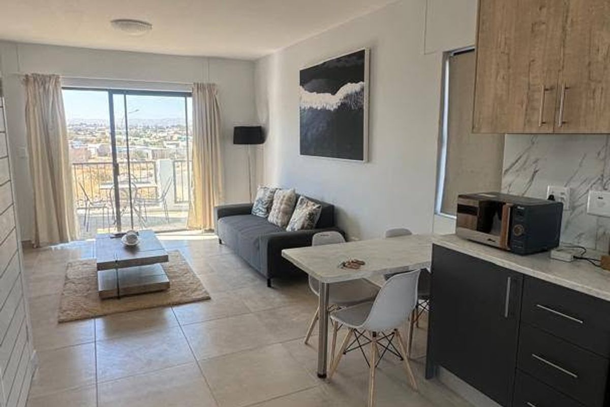 Modern open-plan living area featuring tiled floors, a contemporary kitchen with built-in cabinetry, and a sliding door leading to a balcony with scenic views.