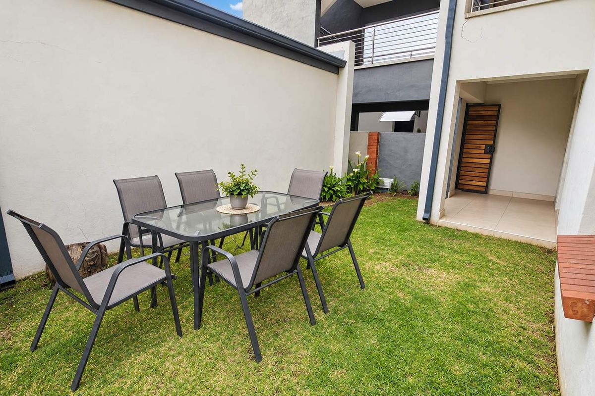 A private rear garden area featuring a well-maintained lawn, boundary wall, and a small tiled patio space adjacent to the building.